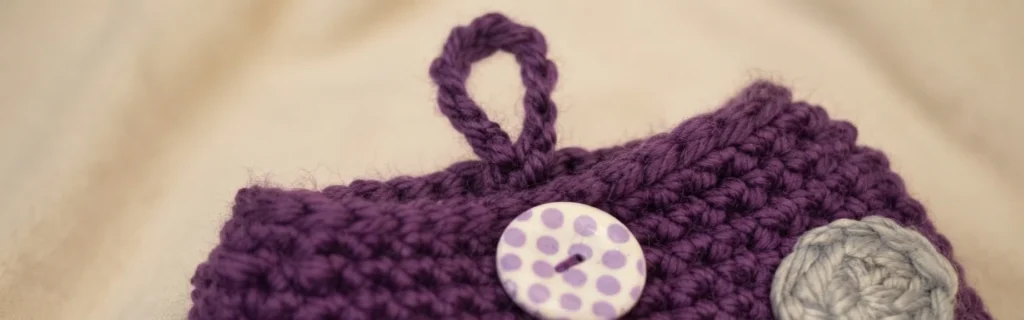 Close-up of a purple crochet mushroom cap with a braided button loop, a white button with purple dots and a grey crochet spot