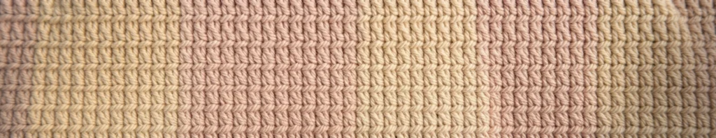 Close-up of a crocheted or knitted fabric texture with narrow vertical stripes alternating cream and pale pink