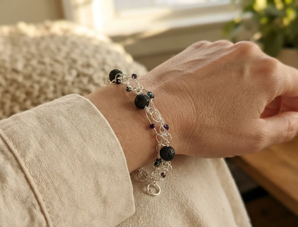 Silver wire-crocheted bracelet with black lava rock beads and small iridescent seed beads, worn on a wrist.