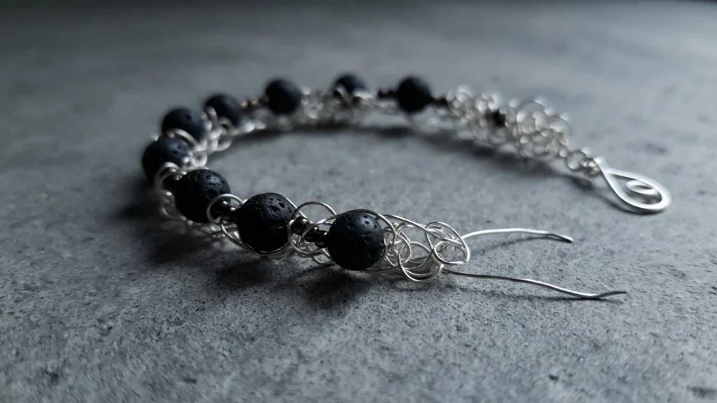 Finished wire crochet bracelet with black lava beads and small seed beads on silver wire, lying on a grey surface.