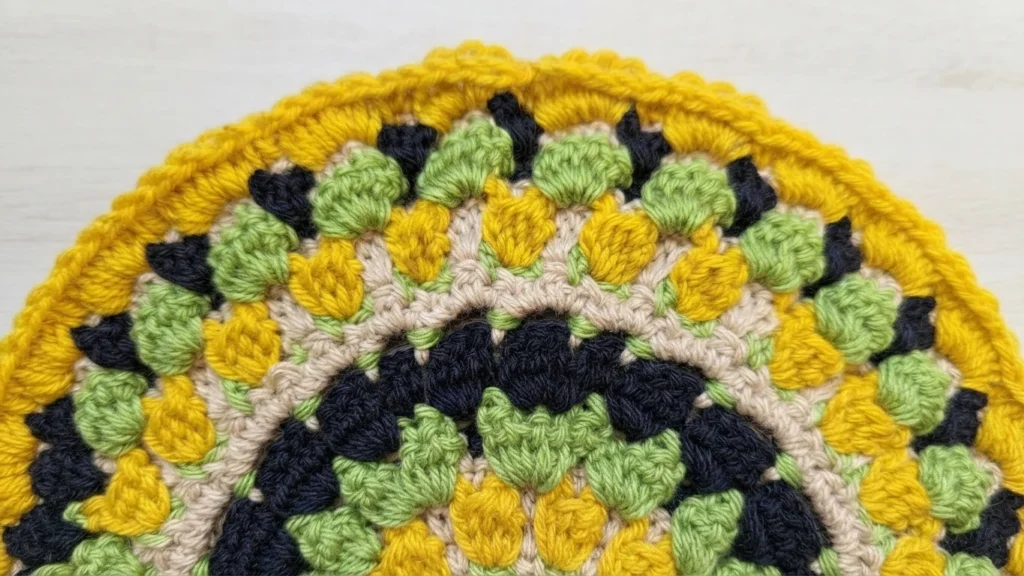 Close-up of a crocheted mandala edge with a yellow border and green, yellow, navy and cream motifs