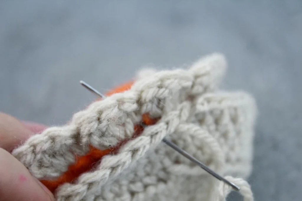 Main tenant une tarte en crochet partiellement assemblée, avec une croûte beige cousue à l'aiguille au-dessus d'une base orange et une petite pointe de crème blanche.