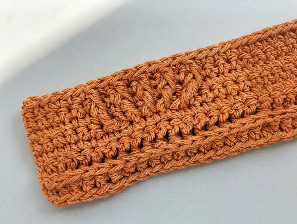Panneau crocheté orange en mailles relief avant, posé à plat et de biais sur une surface claire, une répétition du motif texturé visible.