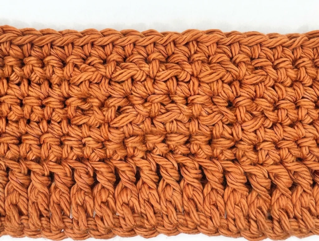 Close-up of an orange cotton crochet panel showing rows of single crochet with raised front post stitches creating a textured pumpkin motif.