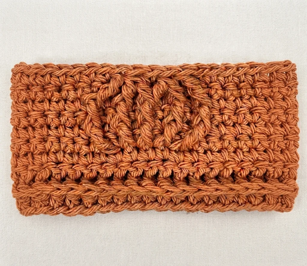 Flat rectangular orange cotton crochet panel with raised front post stitch texture forming a diamond motif, laid on a light linen background.