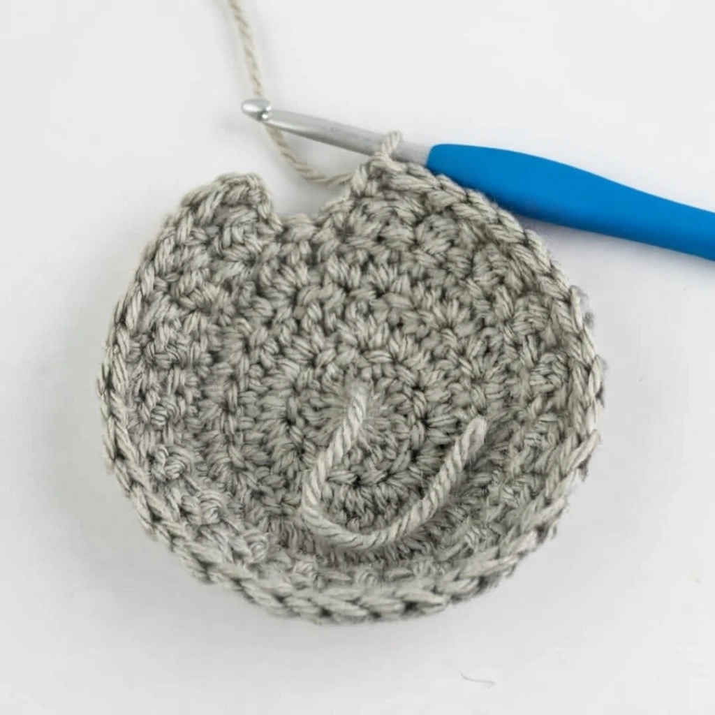 Grey crochet bonnet crown in progress with a blue handled crochet hook on a white background