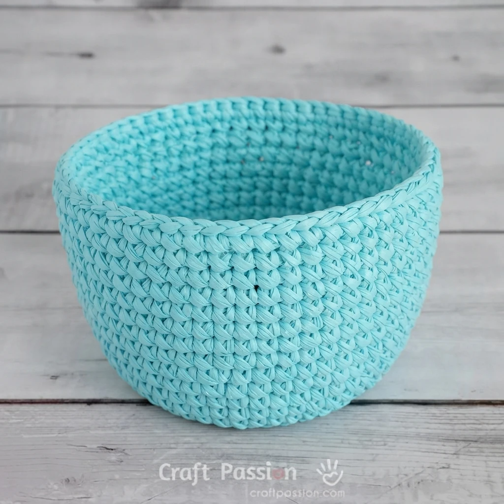 Turquoise crochet raffia base with short upright sides on a light wooden surface.