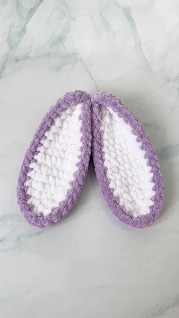 Two crochet bunny ear panels with lilac borders and white centers on a marble surface
