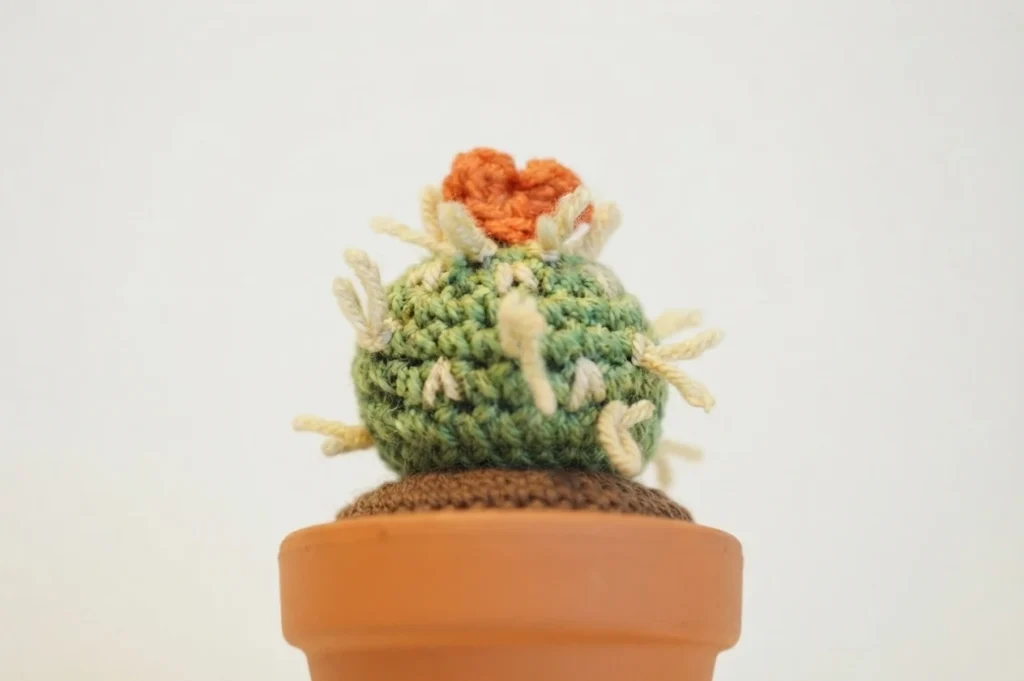 Single crocheted green cactus with cream spines and an orange heart on top in a terracotta pot