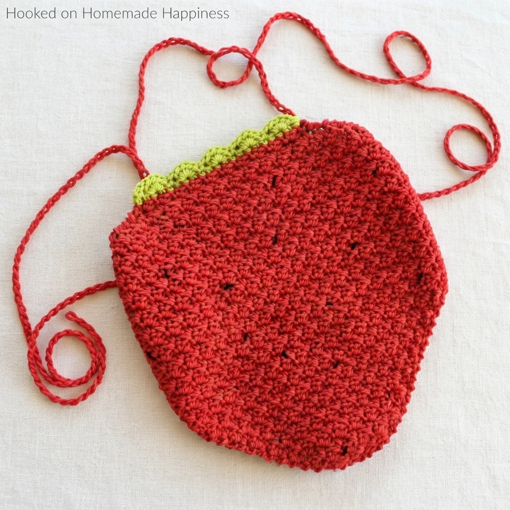 Red crochet strawberry halter top with green scalloped trim, small black seed details, and long red ties laid flat