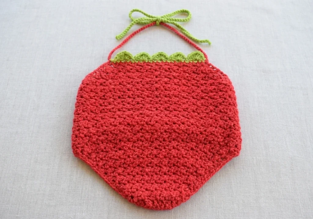 Red crochet halter top with green scalloped trim along the top edge and green tie straps, laid flat on light fabric