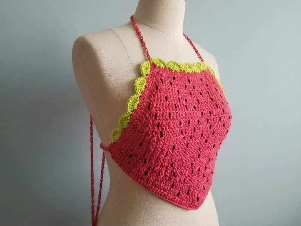 Red crocheted halter top with black seed dots, green scalloped trim and red neck straps displayed on a dress form