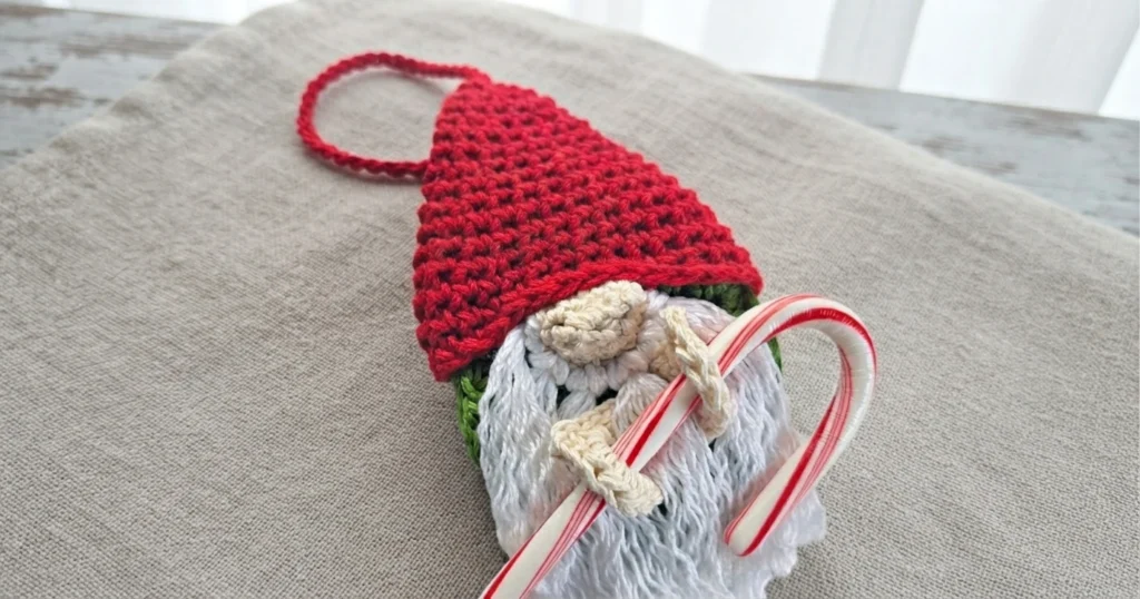 Crocheted gnome ornament with a red hat, white beard, hanging loop, and striped candy cane.