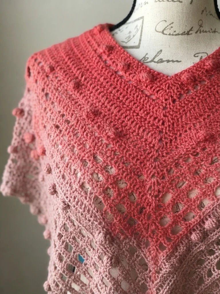 Close-up of a pink gradient crochet poncho with bobble stitches draped on a dress form