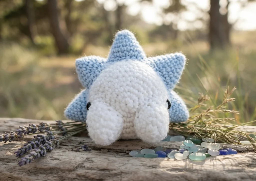 Crocheted Snom amigurumi with white face and light blue spiky shell, photographed outdoors on weathered wood with lavender and sea glass.
