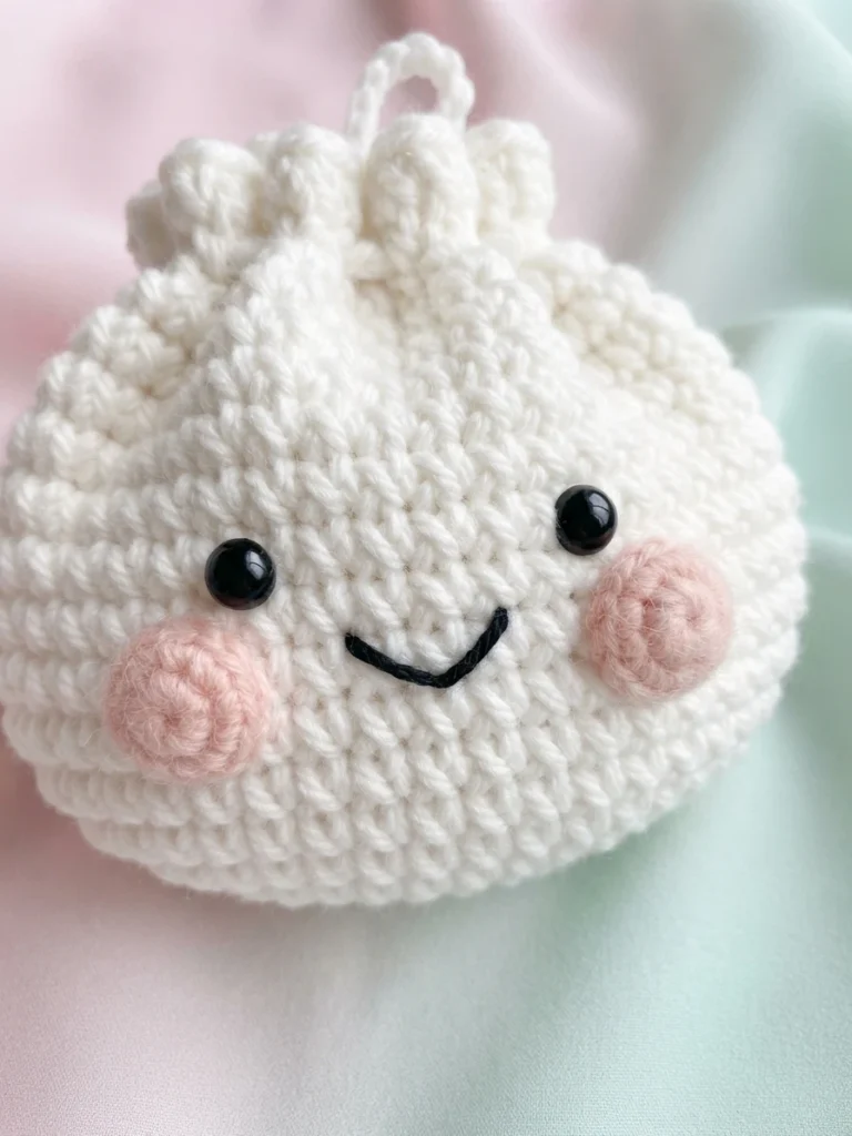 White crochet dumpling bag with black eyes, pink cheeks and a curved smile on pastel fabric.