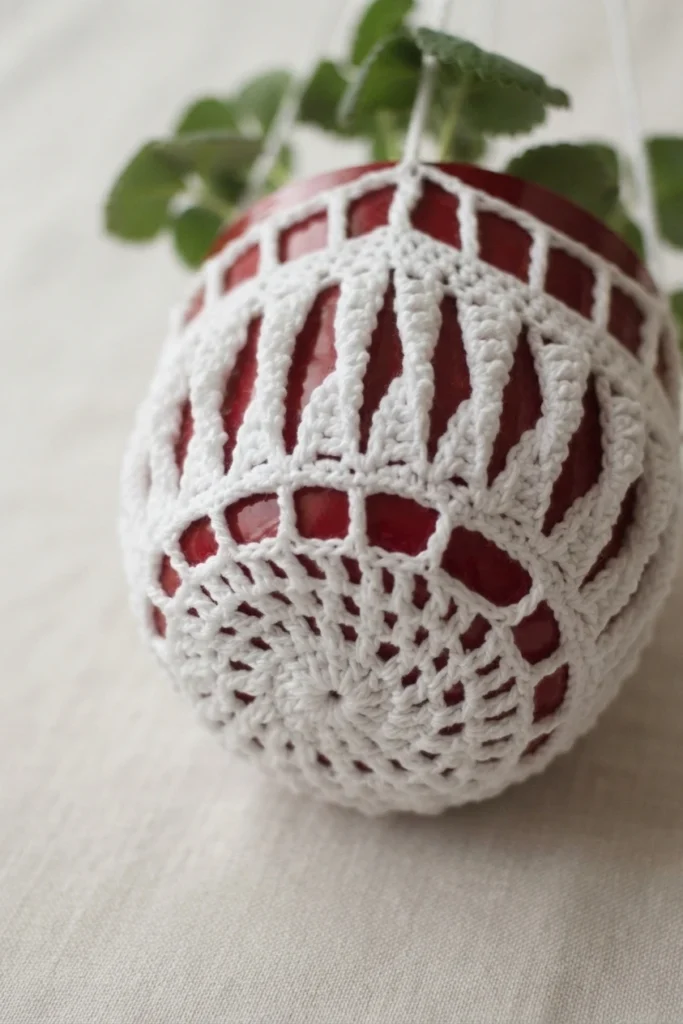 Gros plan d’un cache-pot blanc au crochet autour d’un pot rouge, avec une base ajourée en éventail et une plante verte.