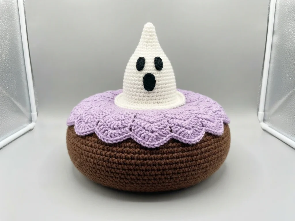 Crochet ghost cupcake with a brown base, scalloped purple frosting edge and a white ghost topper