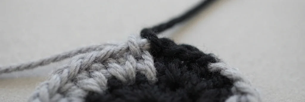 Close-up of black and light grey crochet stitches at a colour change with loose yarn tails on a pale background