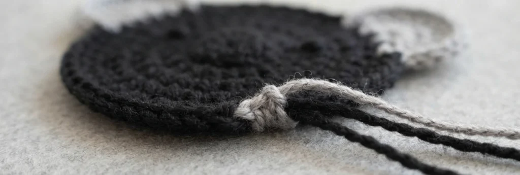 Close-up of a black crocheted circle with a light grey slip knot tied at the edge and black and grey yarn tails extending to the right
