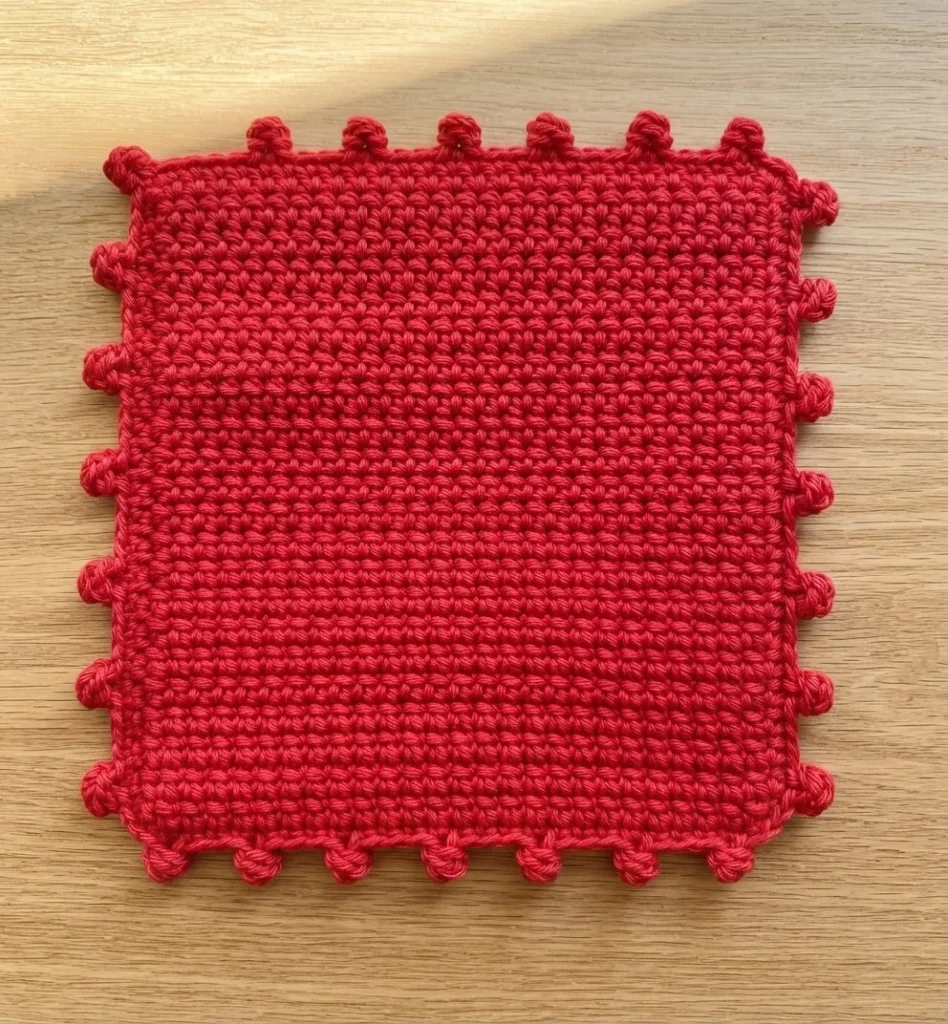 Dessous de plat carré au crochet entièrement rouge, avec une bordure à picots, posé sur une surface en bois.