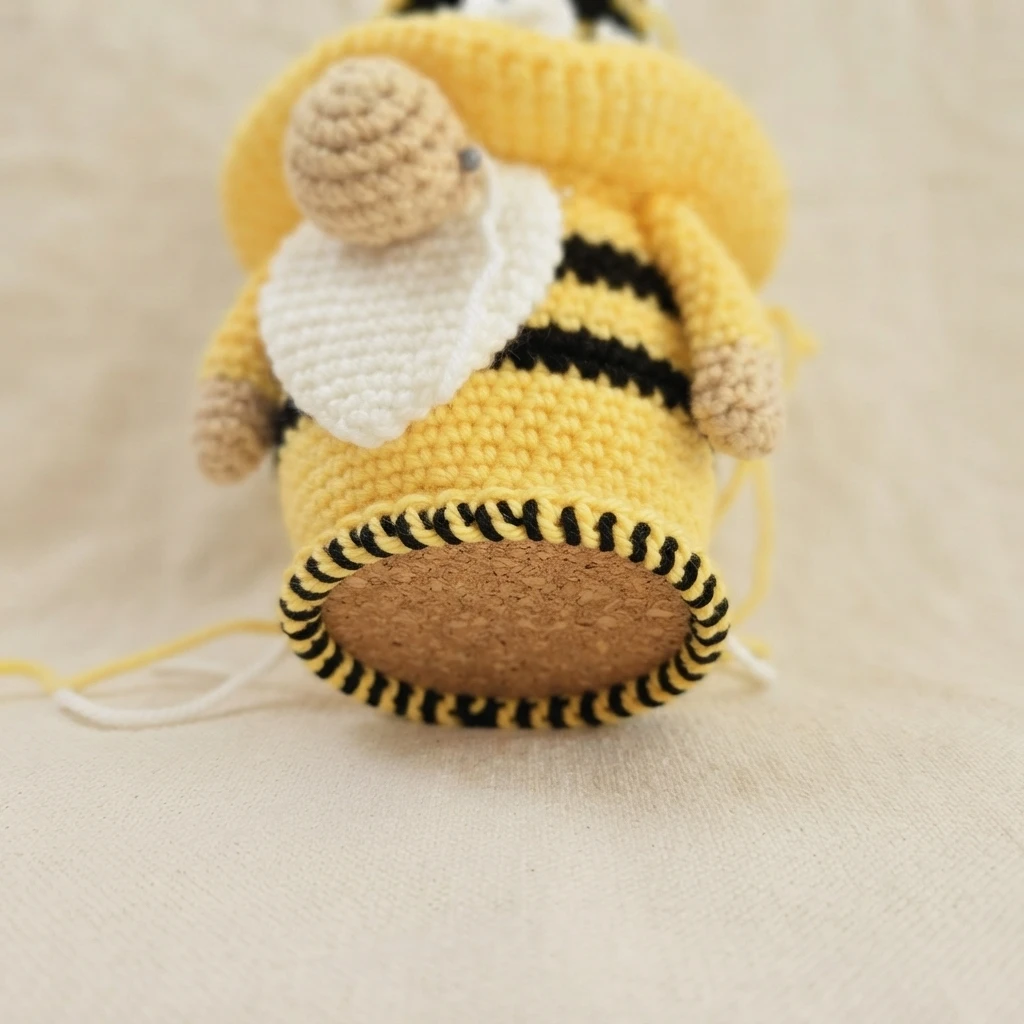 Close-up of the bottom of a crocheted bumble bee gnome showing the finished black and yellow slip-stitch edging around the cork base.