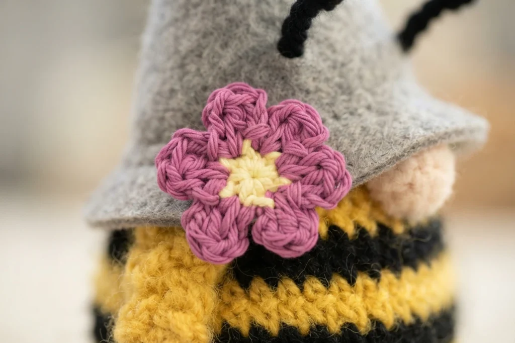 Close-up of a crocheted pink six-petal flower applique with a yellow center pinned to a gray gnome hat.