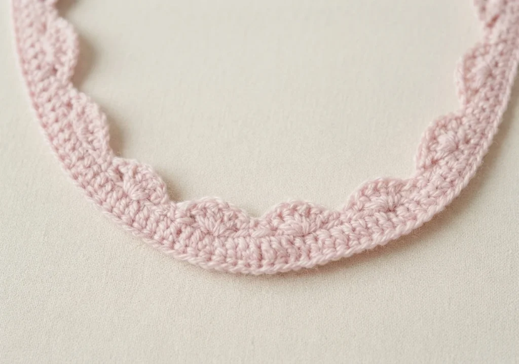 Close-up of a pale pink crocheted scalloped edging strip arranged in a curve on a light cream fabric background