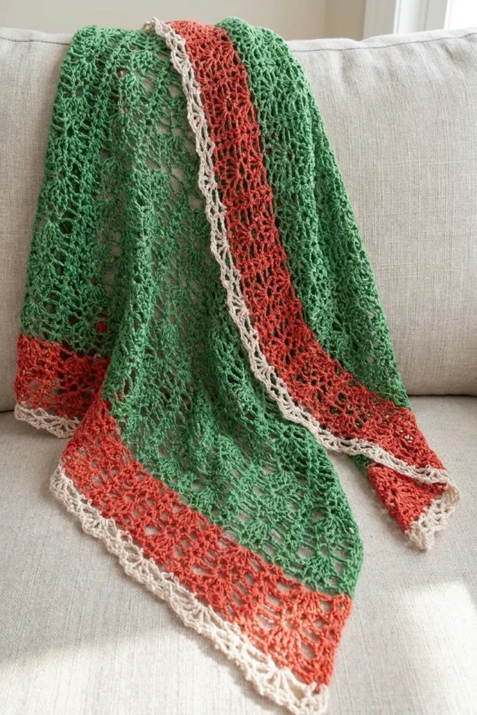 Green, rust red and cream pineapple lace crochet shawl with scalloped edge draped over a light sofa