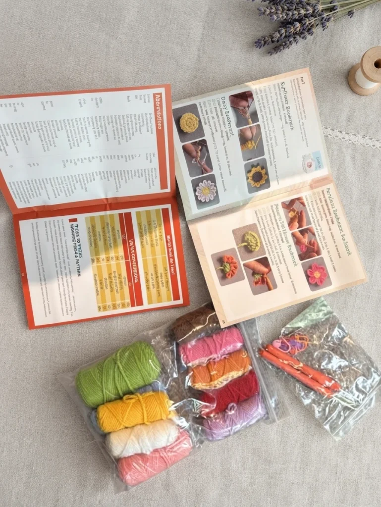 Pelotes de laine colorées, accessoires de crochet et livret ouvert avec des illustrations de fleurs sur un tissu beige.