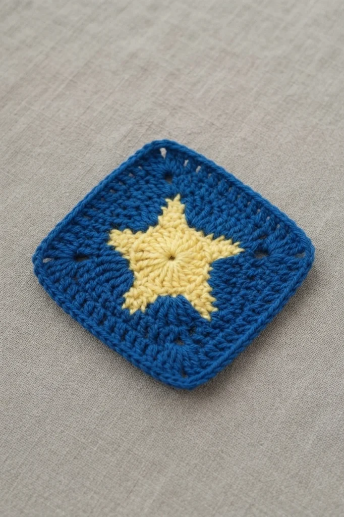 A completed blue granny square with a pale yellow star in the center on beige fabric
