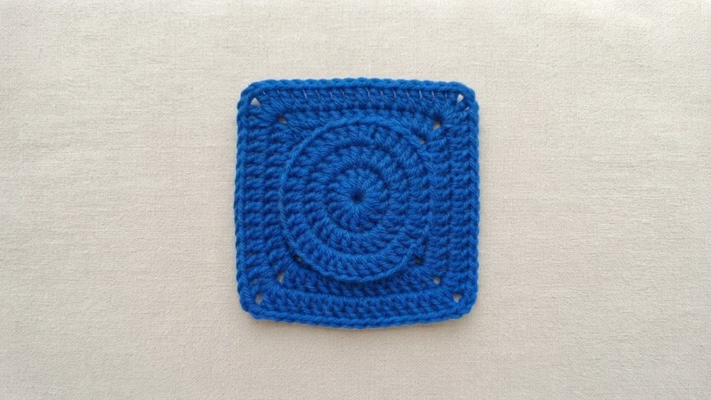 Blue crochet granny square with a circular centre on a beige fabric background
