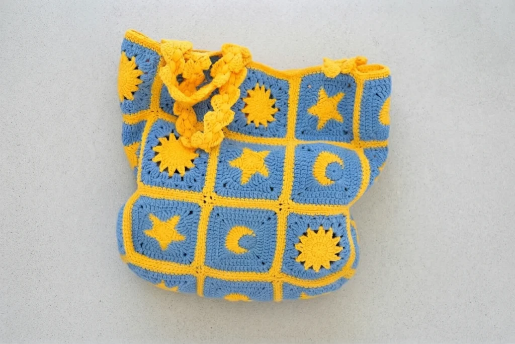 Blue and yellow crochet granny square bag with sun, star and crescent moon motifs and braided yellow straps