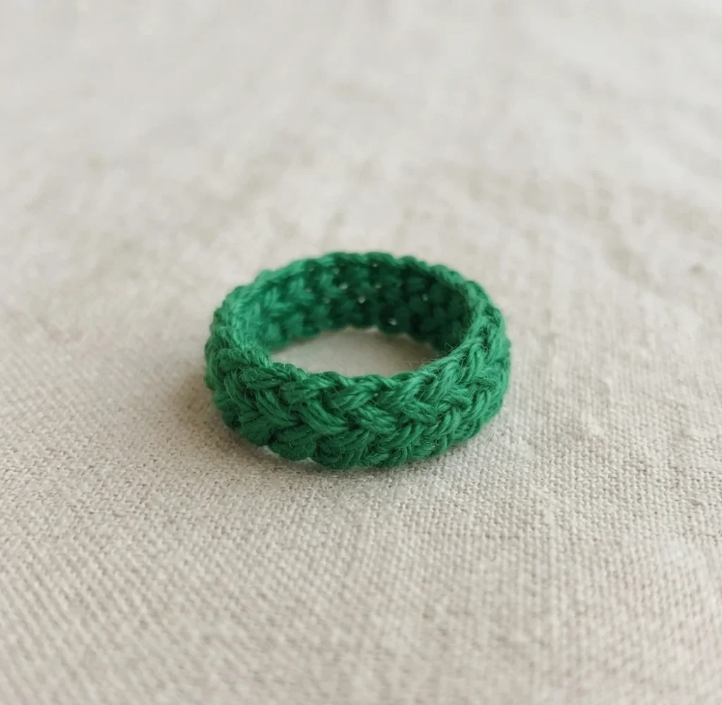 A green crocheted ring lying flat on a light textured fabric surface.