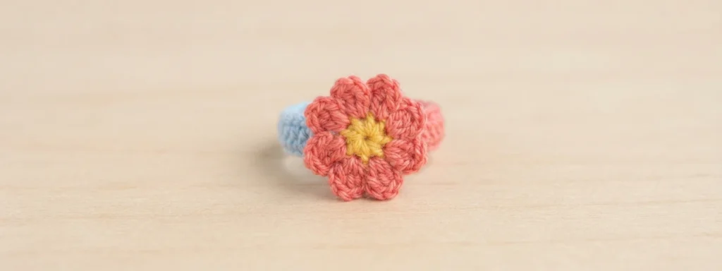 Crocheted flower ring with coral petals, yellow center and light blue band resting on a light wooden surface