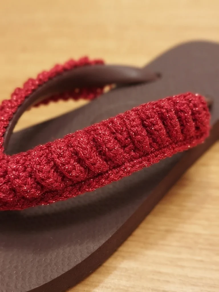 Close-up of a flip-flop with a red crochet covered strap on a light wooden surface