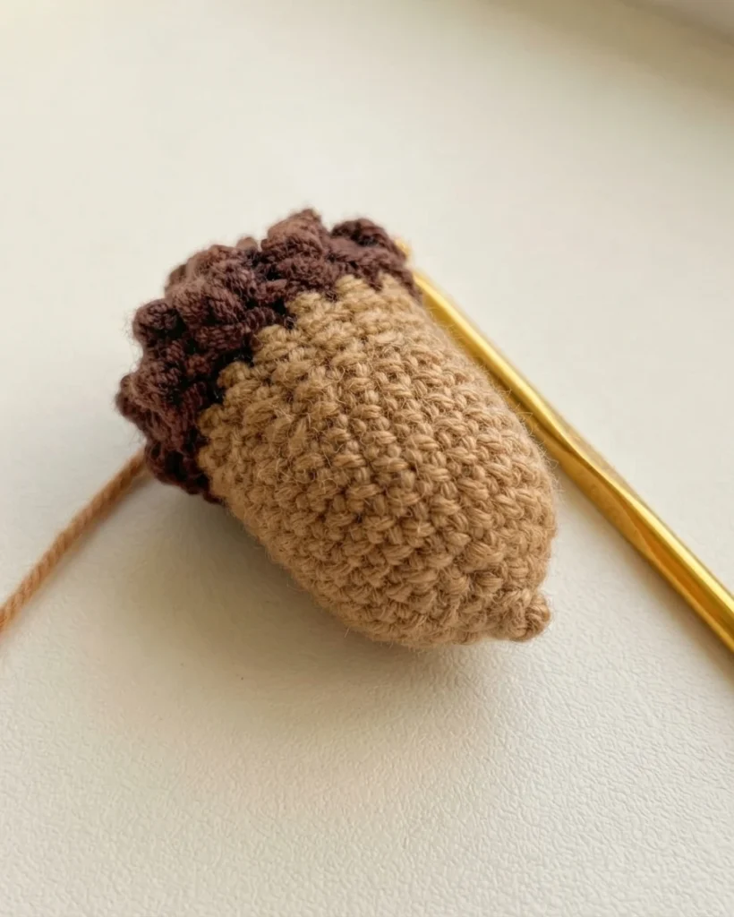 Petit gland au crochet brun et beige, fermé, avec un crochet doré posé à côté.