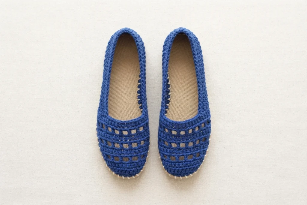 Pair of blue crochet slip-on shoes with openwork toes and light soles, seen from above on a plain light background.