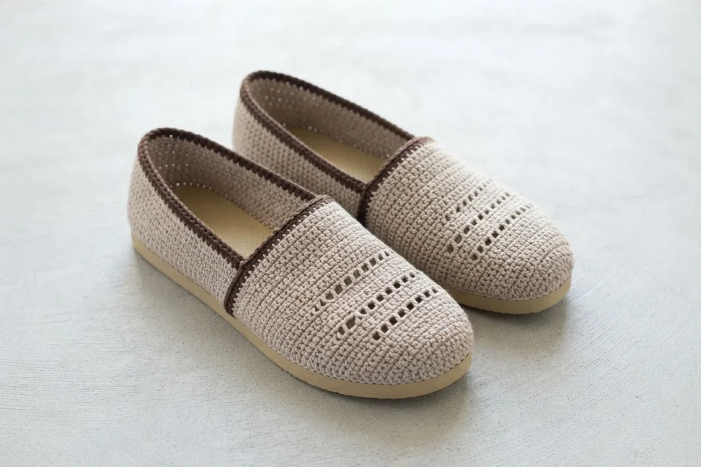 Person presenting finished crochet slip-on shoes with tan flip flop soles and brownish gray striped uppers, with a text overlay reading Crochet Flip Flop Shoes, 10 easy free patterns.