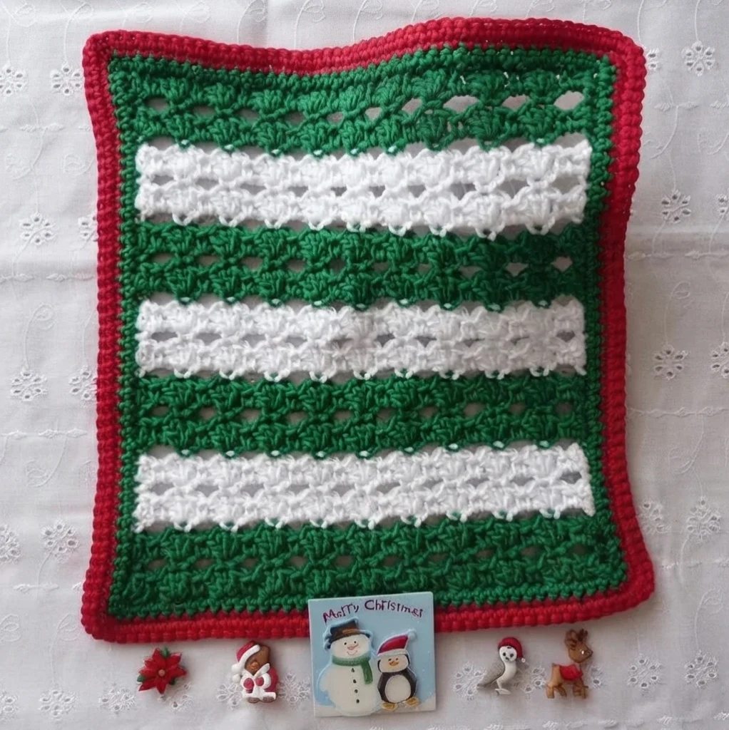 Crocheted Christmas dishcloth with green and white stripes and a red border, styled with small Christmas ornaments