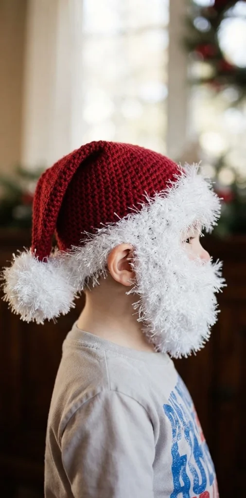 Child wearing a red crocheted Santa hat with a fluffy white beard, side view