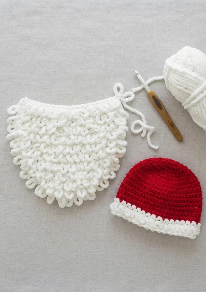 Flat lay of a white double loop crochet Santa beard and red crochet beanie with white brim, beside a crochet hook and ball of white yarn.