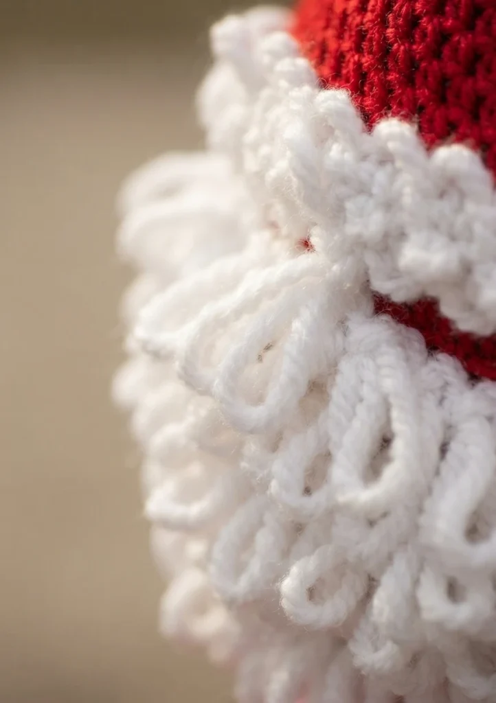 Close-up of white double-loop crochet stitches forming the beard and brim of a red Santa hat