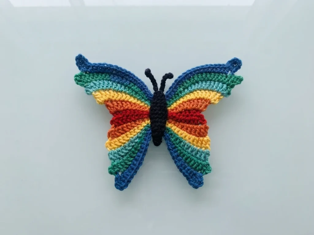 Crochet butterfly with rainbow-striped wings and a black body on a light background