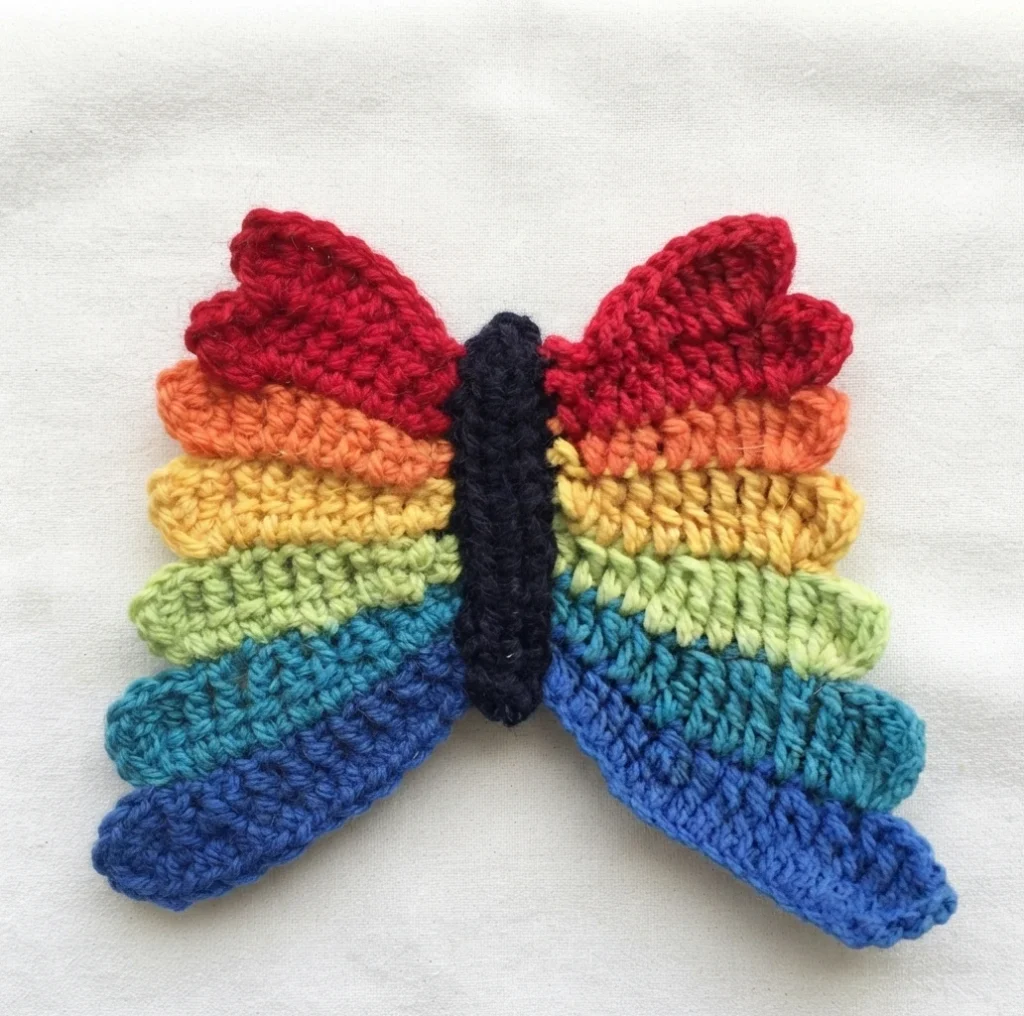 Crocheted rainbow butterfly with dark body on white fabric background