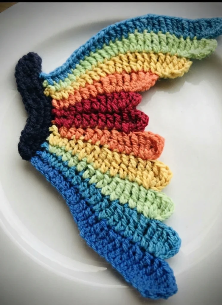 Crochet butterfly wing with rainbow bands and a dark body edge, placed on a white plate
