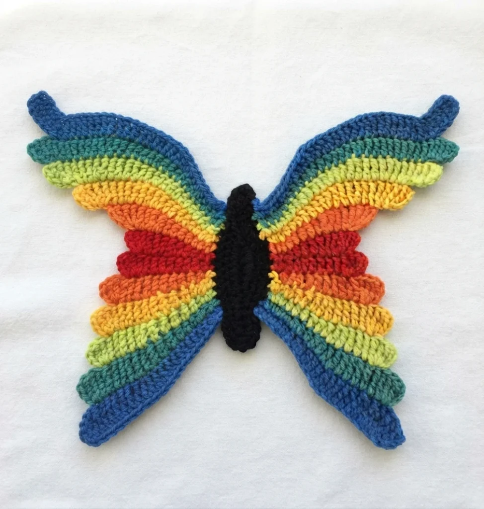 Crochet rainbow butterfly with striped wings in blue, teal, lime, yellow, orange and red and a black body