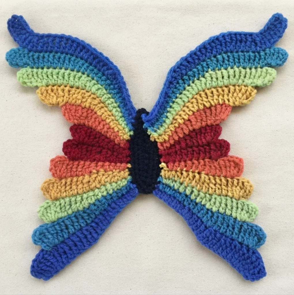 Crocheted butterfly with rainbow striped wings and a dark body on a light background