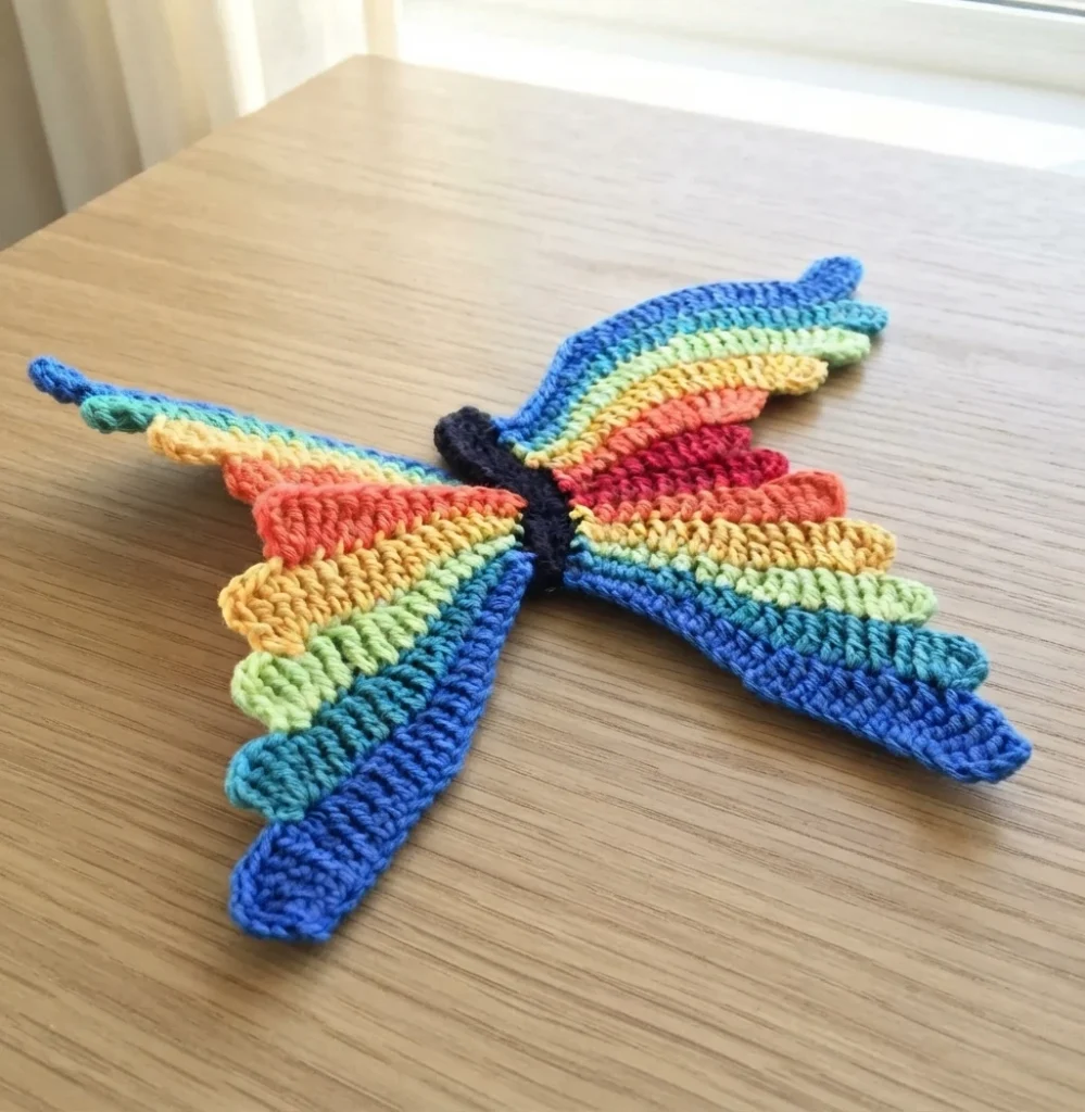 Crochet butterfly with rainbow striped wings and black body on a light wooden table