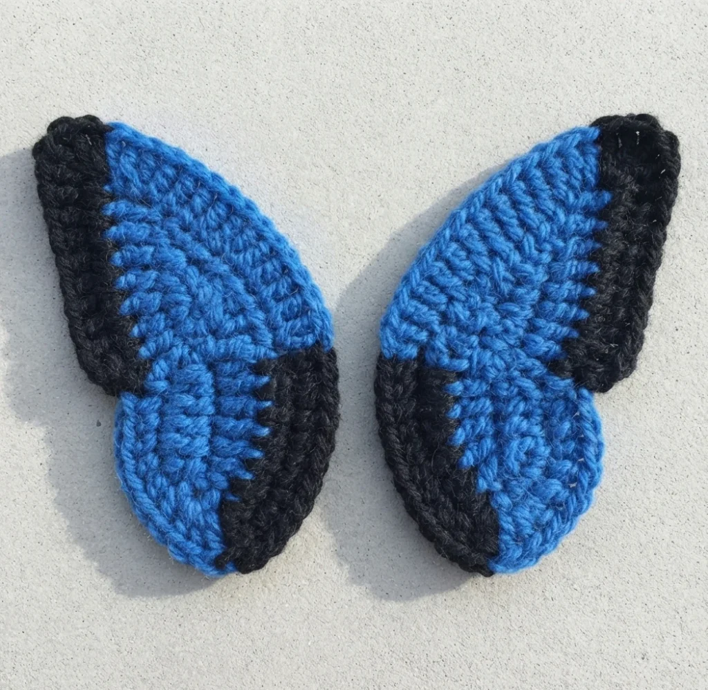 Two crocheted blue wing pieces with black edging side by side on a light neutral background.